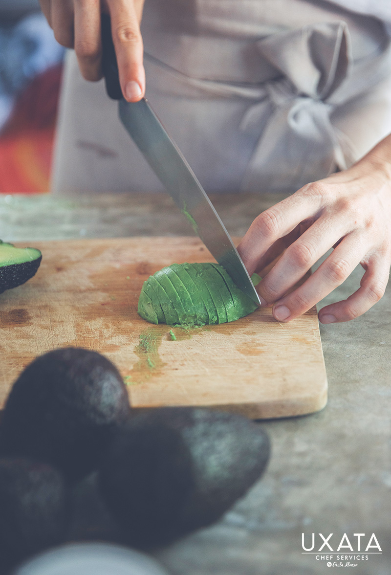 Chef Paula Alonso from UXATA Chef Personal reeling an avocado on a wooden board.