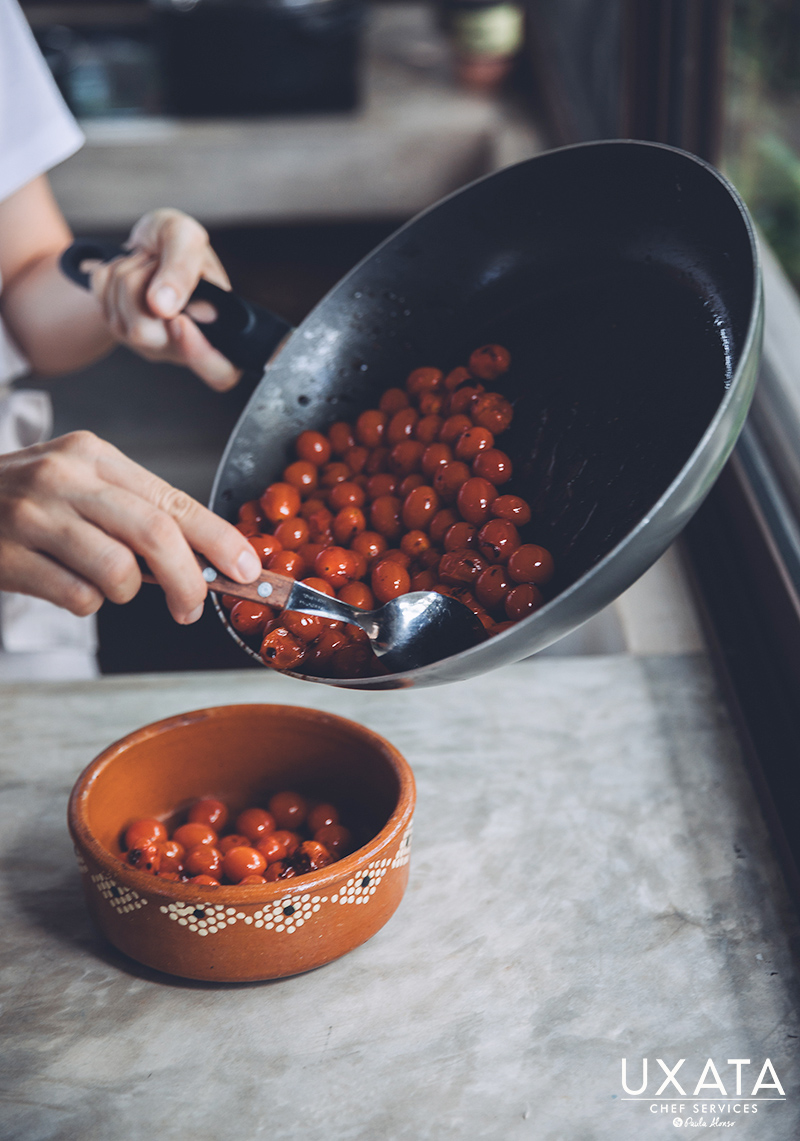 Chef transferring sautéed cherry tomatoes from a frying pan to a bowl.